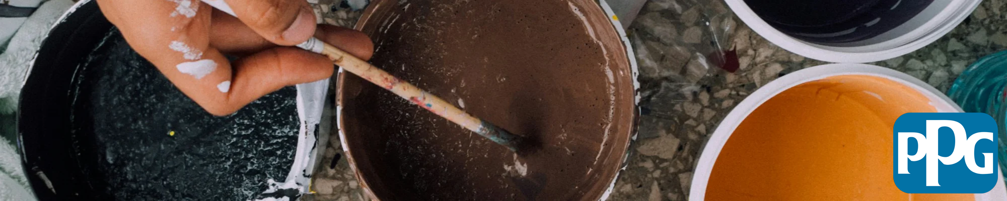 person dipping paintbrush in a can of paint